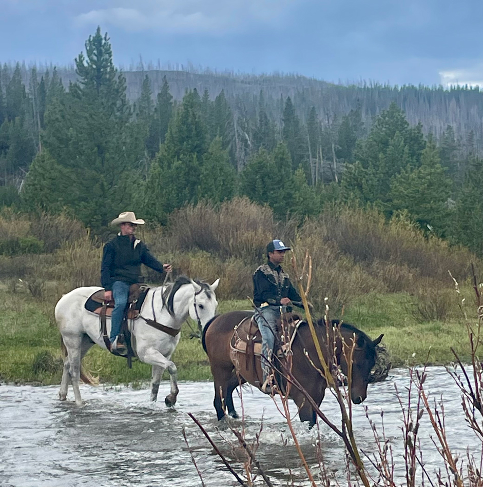 Two boys atop horses crossing a river