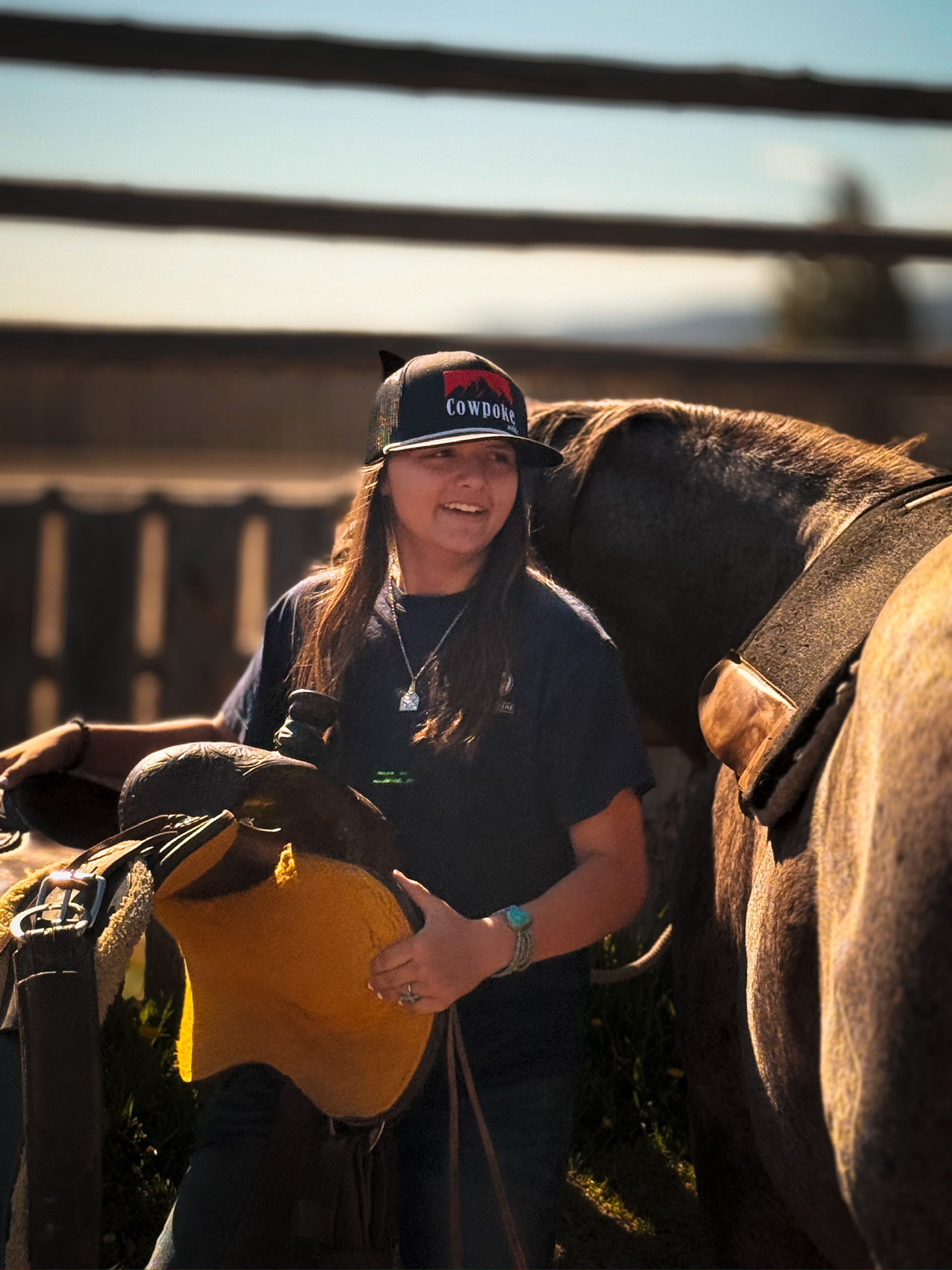 Young woman holding a saddle next to a horse